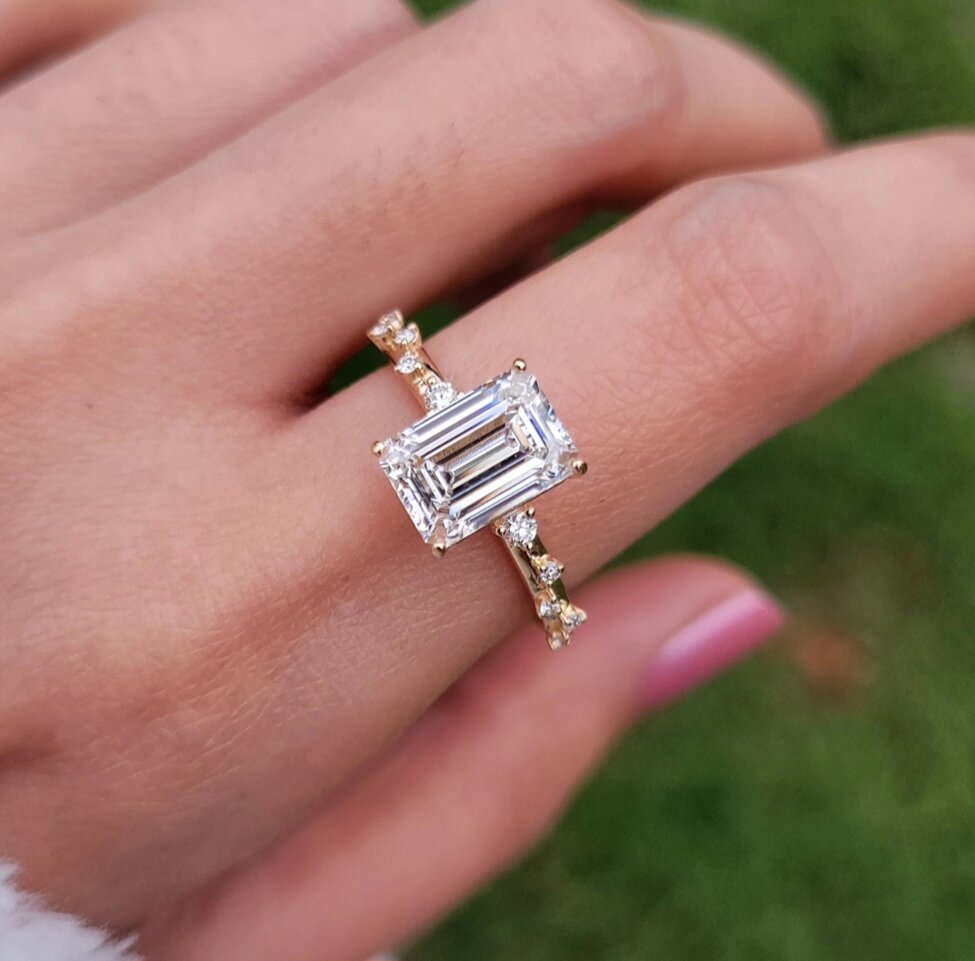A Gemnomads engagement ring featuring a rectangular emerald-cut diamond set in a yellow gold band with small accent diamonds.