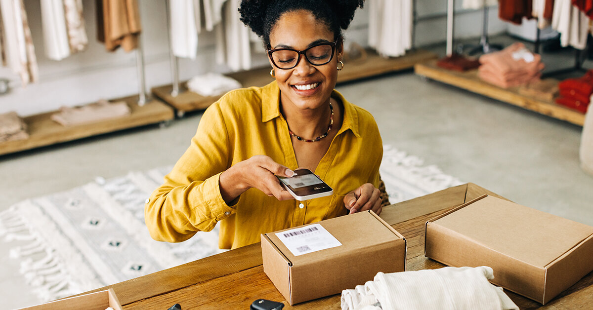 Woman uses a phone to scan a QR code on a box before shipping it.